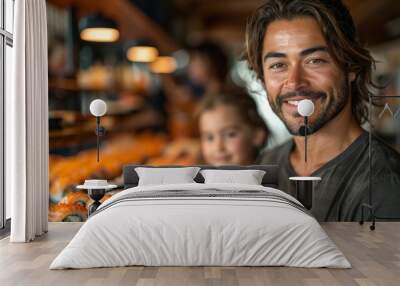 Happy smiling man with long brown hair and beard looking at camera with blurred background of girl and sushi on counter. Wall mural