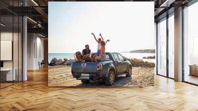 A group of handsome models is having a good time in the back of a car by the sea while listening to the music. Summer, sea, vacation, friendship Wall mural