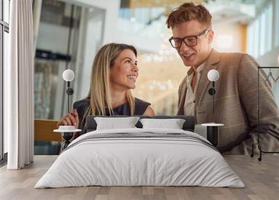 A young business woman is glad showing a laptop content to her young male colleague while standing in the hallway together. Business, people, company Wall mural