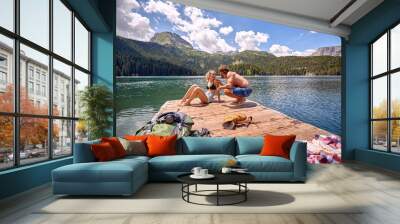 A young couple chatting while sunbathing on the dock at the lake during mountain hiking. Trip, nature, hiking Wall mural