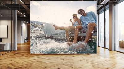 A young couple splashing their legs in the water while sitting at the dock on the seaside. Love, relationship, holiday, sea Wall mural