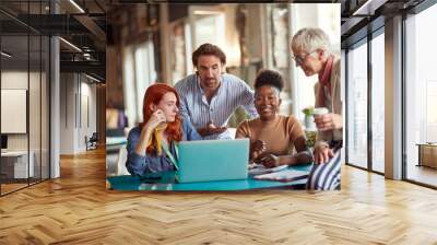 An elderly female boss in the office is watching laptop content with her young colleagues while working together Wall mural