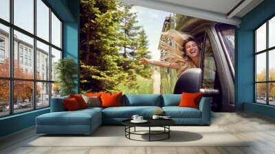 Blonde woman on the window of an rv with hands out smiling enjoying ride. Vacation time. Transport, roadtrip, nature concept. Wall mural