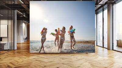 Friends having fun on the beach.Playful girl have fun with water gun at beach at sunny day. Wall mural