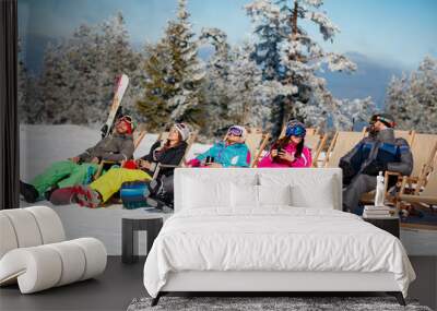 friends sitting with deck chairs in winter mountains. Sunbathing in snow Wall mural