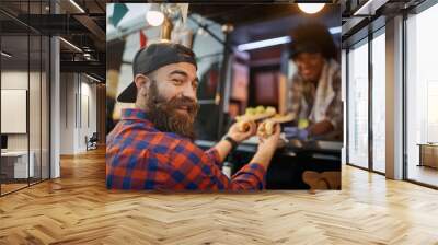 happy, satisfied caucasian male with beard customer receiving sandwiches from a polite employee in fast food service, turning his head, looking at camera, smiling Wall mural