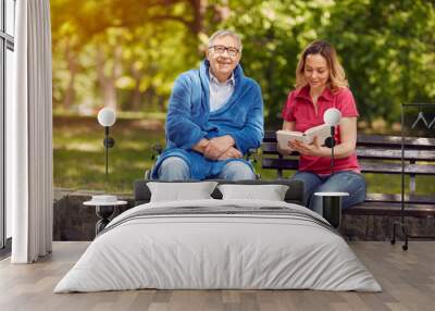 spending time together reading book outdoor daughter and smiling disabled father in wheelchair. Wall mural