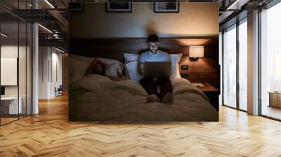 Tired Businessman lying on bed and working with laptop late at night.. Wall mural