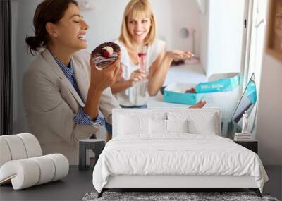 Two beautiful female coworkers eating donuts together Wall mural