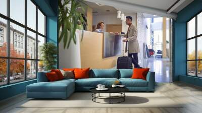 young  afro-american male paying with card to a friendly female caucasian at reception desk Wall mural