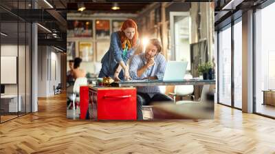 Young colleagues are analyzing documents while working in the office together Wall mural