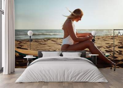 Young sexy girl is sitting on a surfboard and using a smartphone at the beach at sea. Summer, vacation, sea Wall mural