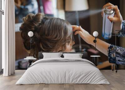 Pretty young bride preparing for wedding at home in the morning. Stylist making hairstyle and apply hairspray on curly hair Wall mural