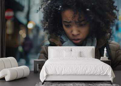 A young black woman looks at her cell or mobile with a look of concern, the victim of revenge porn, blackmail, hate crime or online fraud, 16:9 landscape format with copy space Wall mural