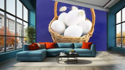 On a blue background, a wicker basket with raw chicken eggs in a shell. Wall mural