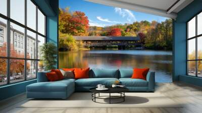 Stunning autumn view of a covered bridge over a calm river with vibrant fall foliage and a clear blue sky. Wall mural