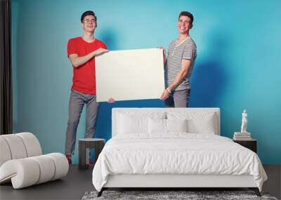 Advertising. Your text here. Couple of handsome young men holding an empty board with copy space together on blue background. Wall mural