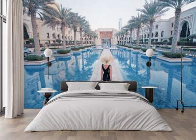 Beautiful young woman in black dress with hat walking on Dubai Downtown. Wall mural