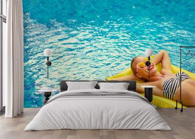 Enjoying suntan. Vacation concept. Slim young woman in bikini on the yellow air mattress in the swimming pool. Wall mural