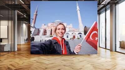 Enjoying vacation in Istanbul. Young traveling woman with national turkish flag taking selfie on view of Hagia Sophia Temple. Wall mural