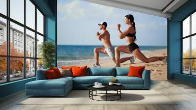 Healthy lifestyle. Young beautiful couple doing sports exercises at the beach. Wall mural