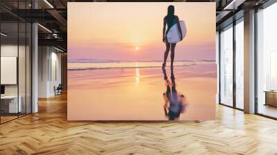 Hobby and vacation. Sunset on the beach. Young woman carrying surf board. Wall mural