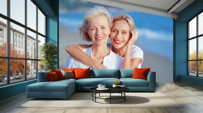 Outdoor close up portrait of smiling happy caucasian senior mother with her adult daughter hugging and looking at the camera on sea beach. Wall mural