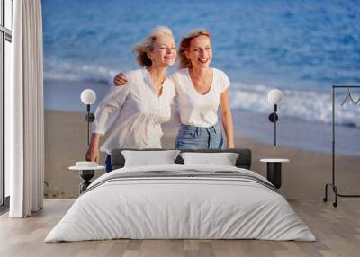 Outdoor portrait of smiling happy caucasian senior mother with her adult daughter hugging and walking on sea beach. Wall mural