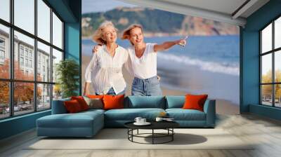 Outdoor portrait of smiling happy caucasian senior mother with her adult daughter hugging and walking on sea beach. Wall mural