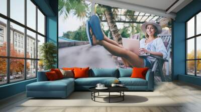 Technology and travel. Working outdoors. Freelance concept. Pretty young woman using laptop in cafe on tropical beach. Wall mural