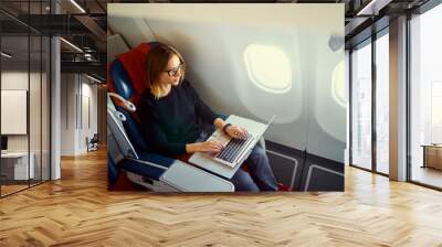 Traveling and technology. Flying at first class. Pretty young businees woman working on laptop computer while sitting in airplane. Wall mural