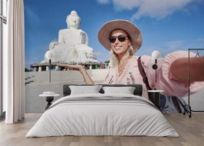 Traveling by Thailand. Pretty young woman in hat taking selfie in the Big Buddha Temple, famous Phuket sightseeing. Wall mural