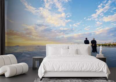 Two priests walking on the sea promenade with wonderful sunset view. Wall mural