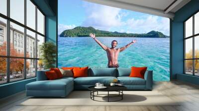 Vacation and freedom. Happy young man rising hands up bathing on tropical beach enjoying beautiful view. Wall mural