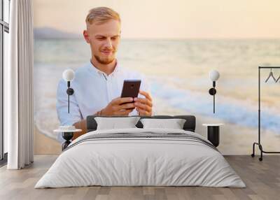 Vacation and technology. Portrait of young handsome man using smartphone on the sea shore. Wall mural