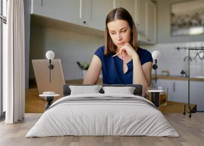 Working at home. Freelance concept. Thoughtful young woman using laptop in kitchen. Wall mural