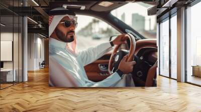 Middle Eastern man in traditional attire driving a luxury car through a city, wearing sunglasses and looking confident, with urban buildings in the background Wall mural