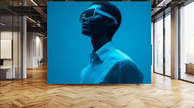 Stylish young man wearing futuristic sunglasses against a blue background with copy space  Wall mural