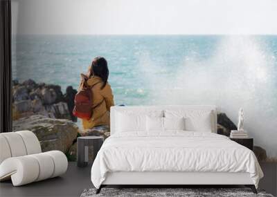 Caucasian traveler woman looking at the waves on the sea with a yellow jacket in Peniche, Portugal Wall mural