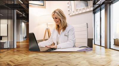 Cheerful doctor using laptop in office Wall mural