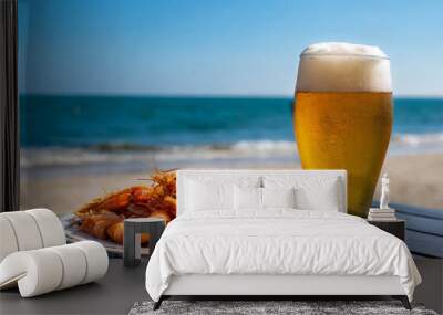 A glass of beer and a portion of fried prawns on a table at the beach Wall mural