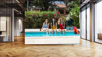 Three girls of different ethnicities with bathing suits of different colors toasting with beer in a pool and with a cassette Wall mural