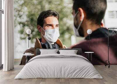 Two gay men with face masks on lovingly looking at each other while one is touching the other's face. Wall mural