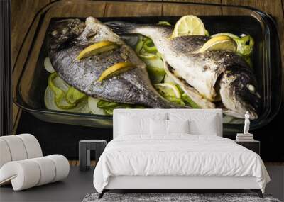 two Dorada fish cooked in the oven with lemon, onion and green pimento in a glass dish on a black slate tray Wall mural