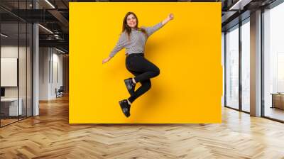 A full-length shot of a Young girl  jumping over isolated yellow background Wall mural