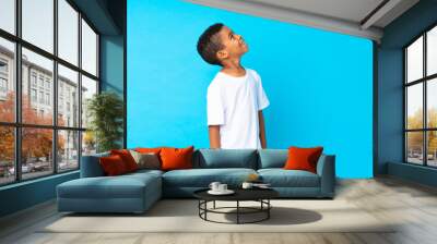 African American boy over isolated blue background looking up while smiling Wall mural