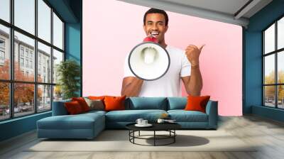 African American handsome man on isolated pink background shouting through a megaphone and pointing side Wall mural