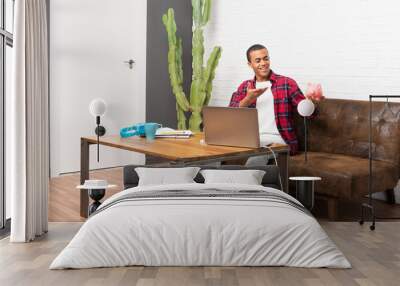 African american man with laptop in the living room holding a big piggybank Wall mural