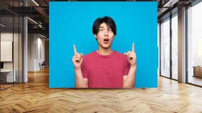 Asian man with red shirt over isolated blue wall pointing with the index finger a great idea Wall mural