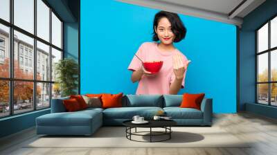 Asian young woman holding a bowl of cereals inviting to come with hand. Happy that you came Wall mural